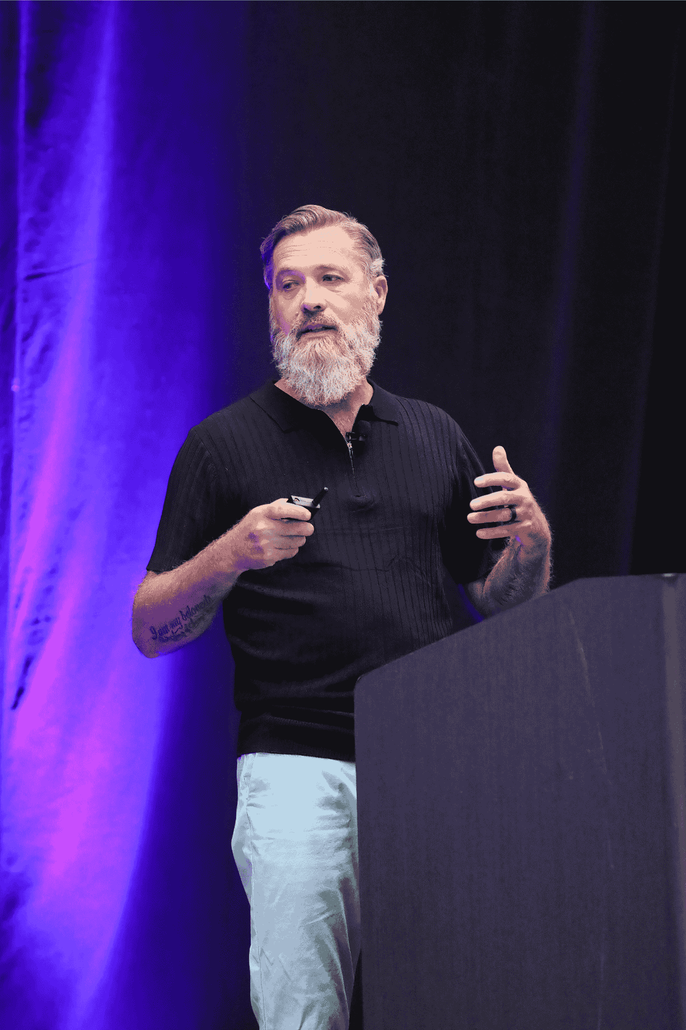Alan Darsey von Clearwave Fiber präsentiert auf der Bühne des IQGeo Americas Meetup 2025 in Dallas vor einem vollen Publikum bei violetter Bühnenbeleuchtung
