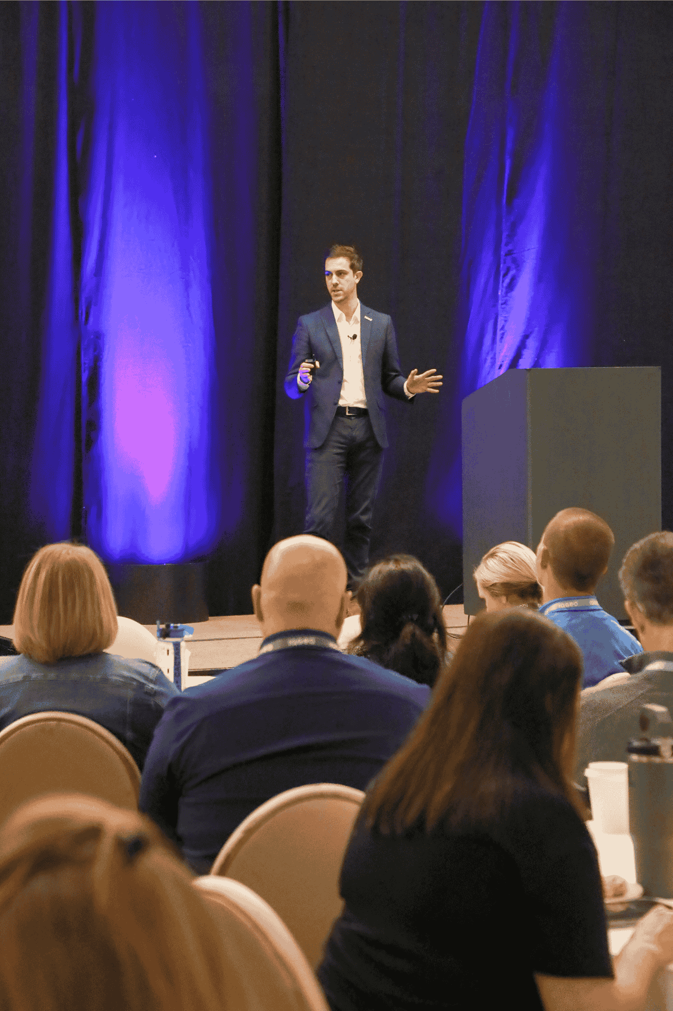 Aloïs Brunel von IQGeo präsentiert auf der Bühne beim IQGeo Americas Meetup 2025 in Dallas vor einem vollen Publikum bei lila Bühnenbeleuchtung