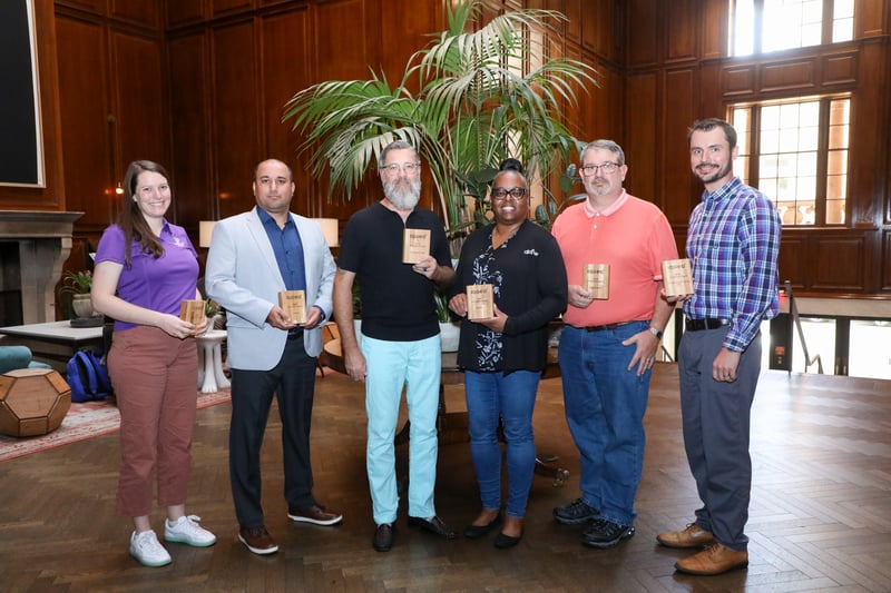 Eine Gruppe von sechs Personen, die beim IQGeo Americas Meetup 2025 hölzerne Preisplaketten halten, um die Gewinner von Kunden- und Partnerinnovationen zu feiern.