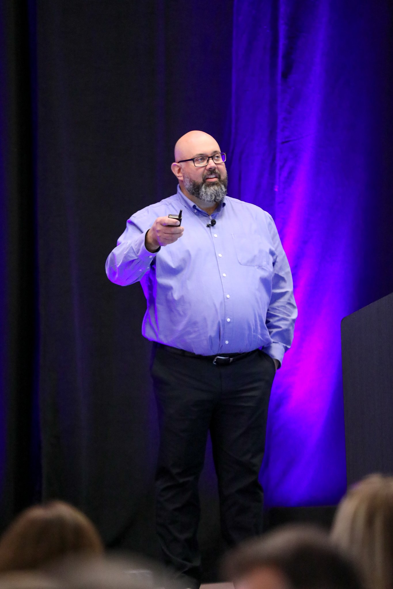 Jason Lemon von SaskTel präsentiert auf der Bühne beim IQGeo Americas Meetup 2025 in Dallas vor einem vollen Publikum bei lila Bühnenbeleuchtung