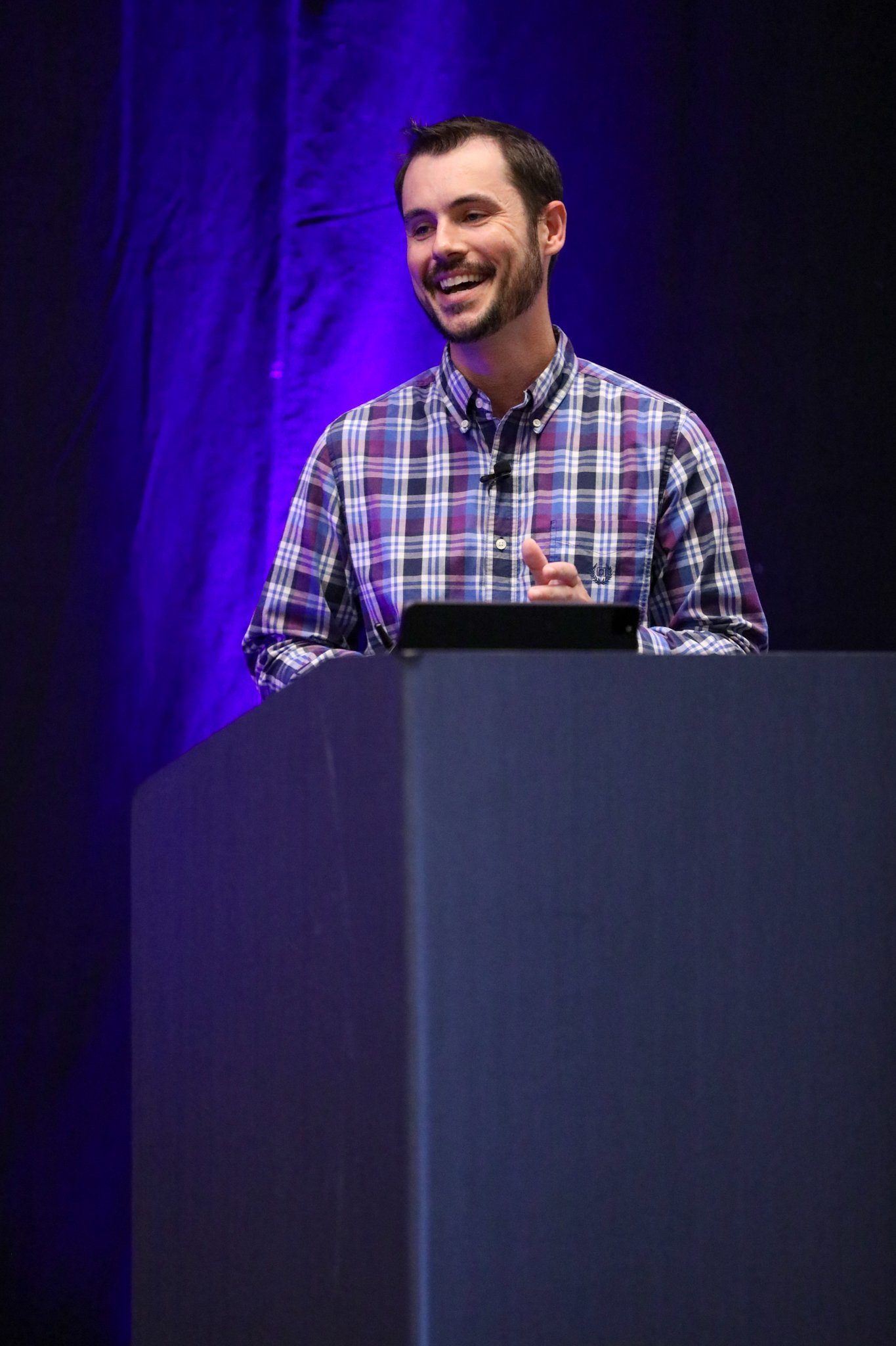 Ryan Cox von PPL präsentiert auf der Bühne beim IQGeo Americas Meetup 2025 in Dallas vor einem vollen Publikum bei lila Bühnenbeleuchtung