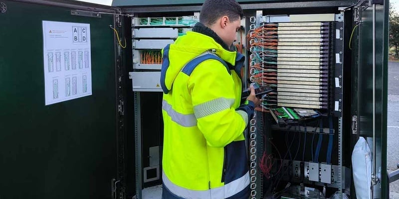Ein Telekommunikations-Außendiensttechniker in einer Warnweste, der in einem geöffneten Telekommunikationsschrank Kabel anschließt.